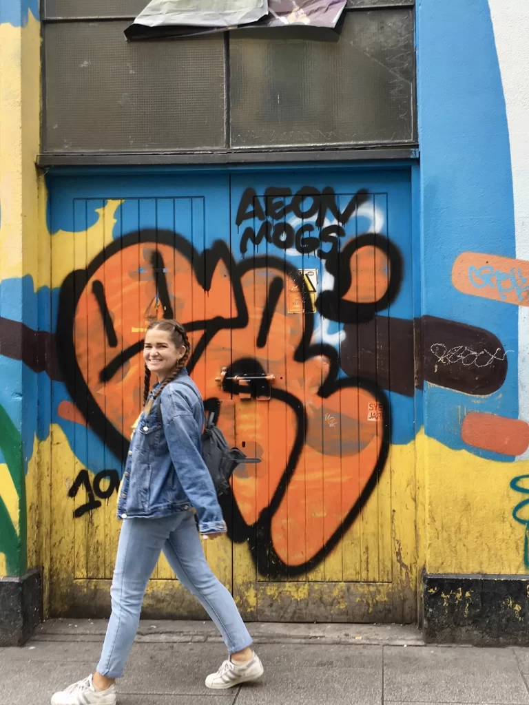 Niki walks in front of a graffitied wall in Dublin