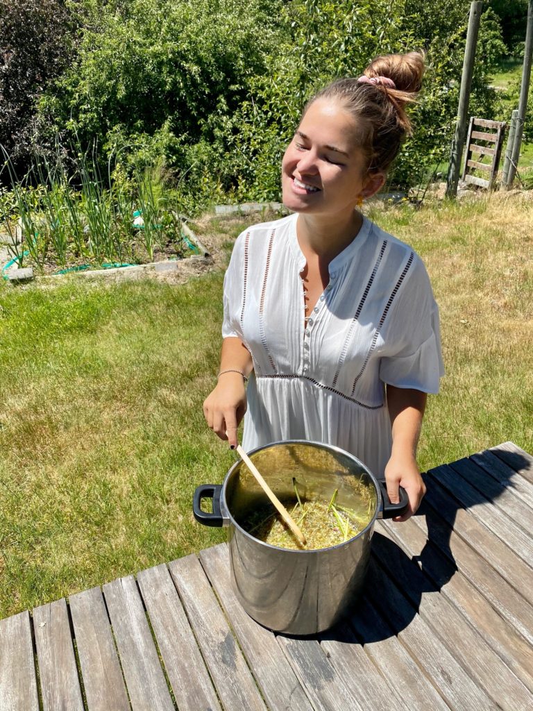 how to make elderflower cordial: niki poses outdoors with a pot of elderflower cordial