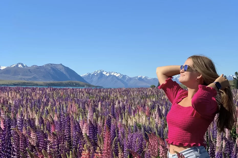 niki stands in a field of lupins with snow-capped mountains behind her