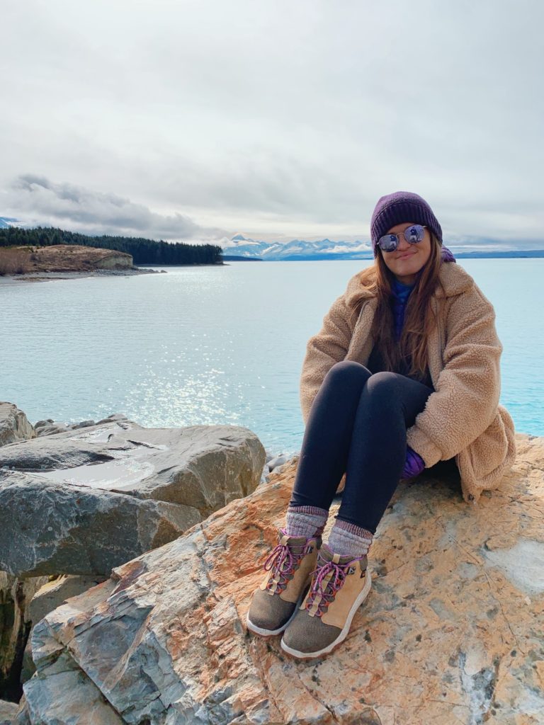 pros and cons of living in new zealand: niki sits in front of lake pukaki in the winter