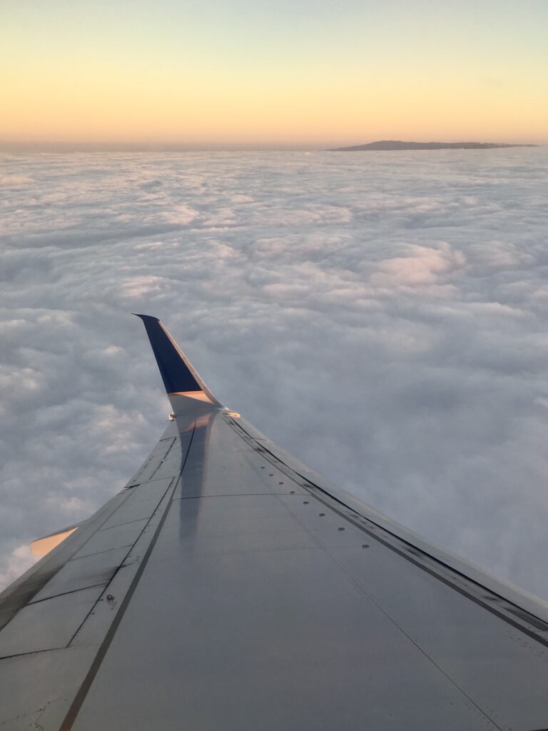long-haul flight essentials: airplane wing over a blanket of clouds during sunset