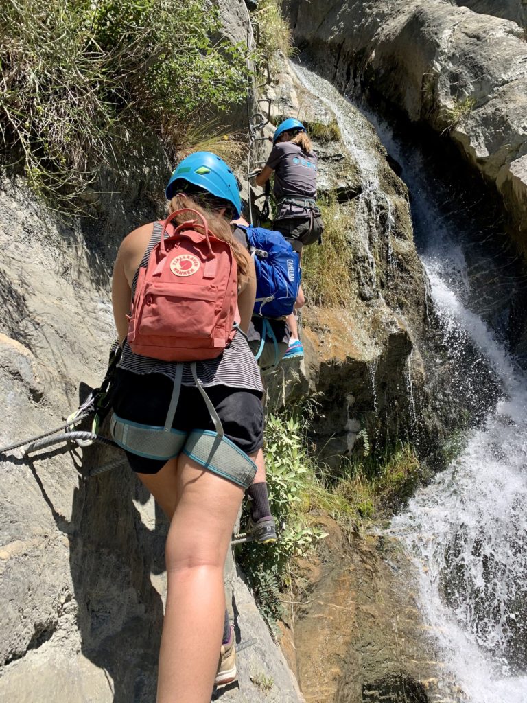 niki climbs up a via ferrata with waterfall in background