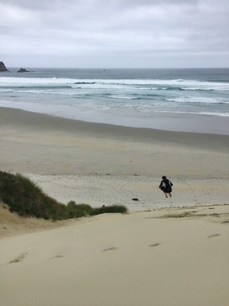 ben jumping over sand dunes at sandfly bay