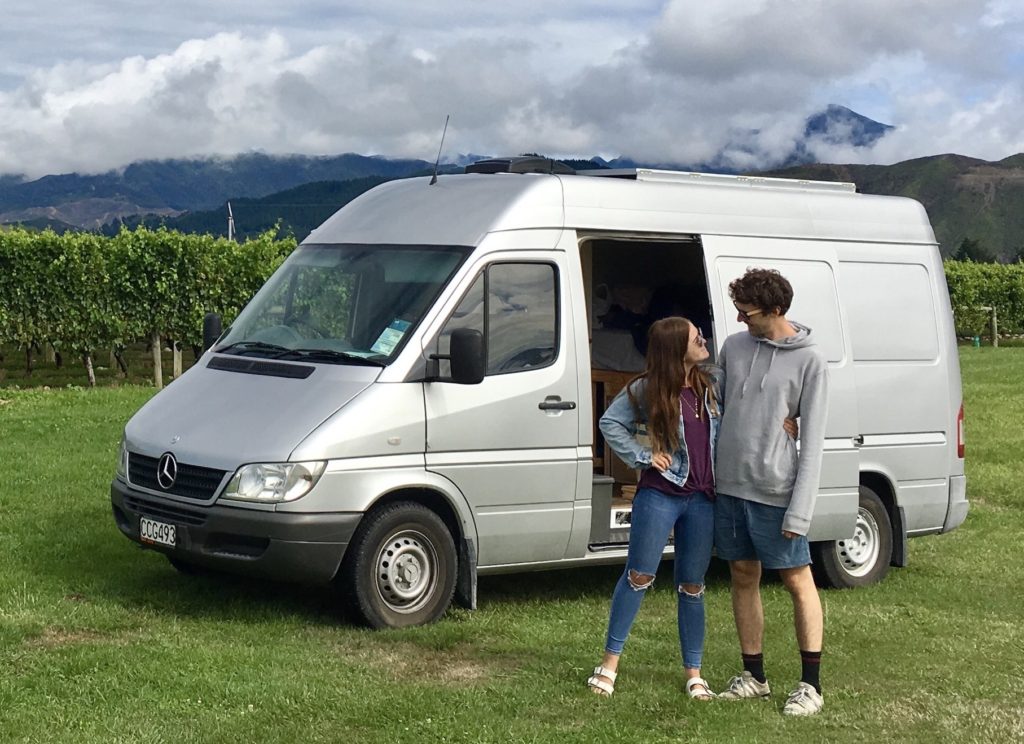 Niki and Ben stand in front of their van in New Zealand