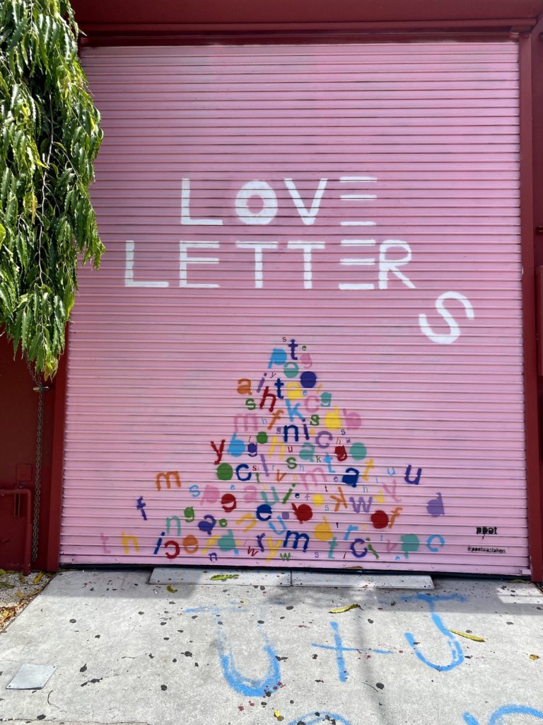 Street art on a pink background that says "Love letters" with a mountain of colorful alphabet letters