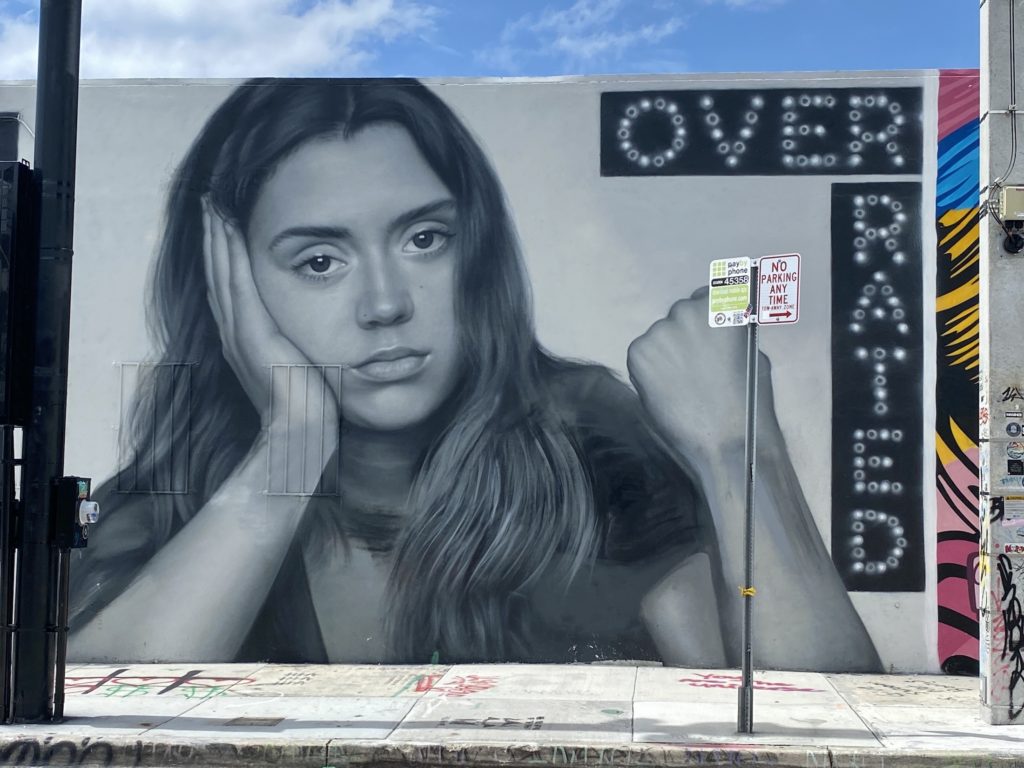 Street art with a bored looking young woman and the word "overrated"