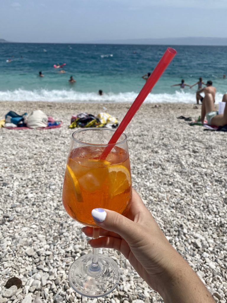 Split travel guide: Niki holds up an aperol spritz drink at Znjan city beach, Split, Croatia