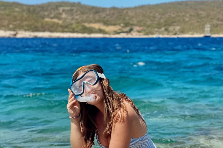 Niki, wearing snorkeling gear, squats on a rock in front of blue water on Vis island, Croatia