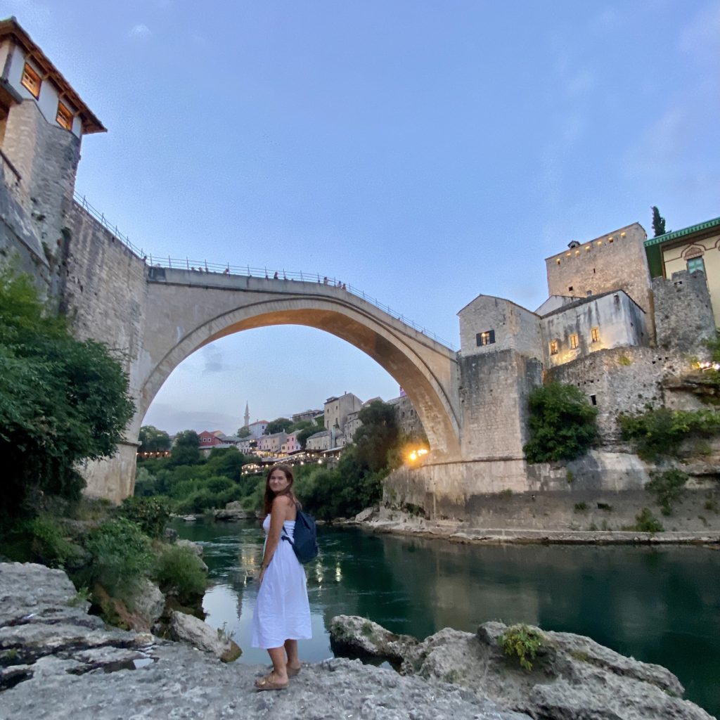 Niki stands on the bank of the river in front of Stari Most (Old Bridge), Mostar, Bosnia & Herzegovina