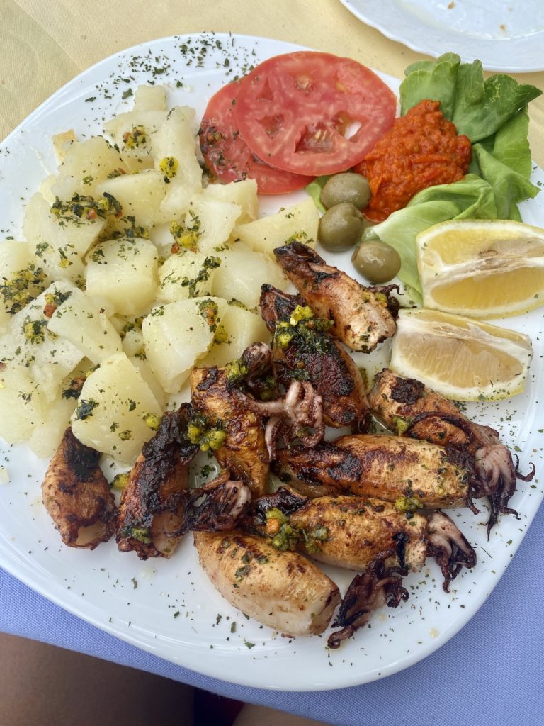 Plate of grilled squid, boiled potatoes, tomato slices, olives, lettuce, and roasted red pepper sauce at Konoba Goldfish Restaurant, Blagaj, Bosnia & Herzegovina