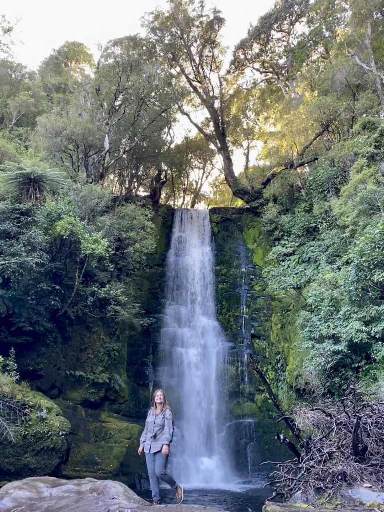 South Island New Zealand road trip: Niki stands in front of a waterfall, the Catlins, New Zealand