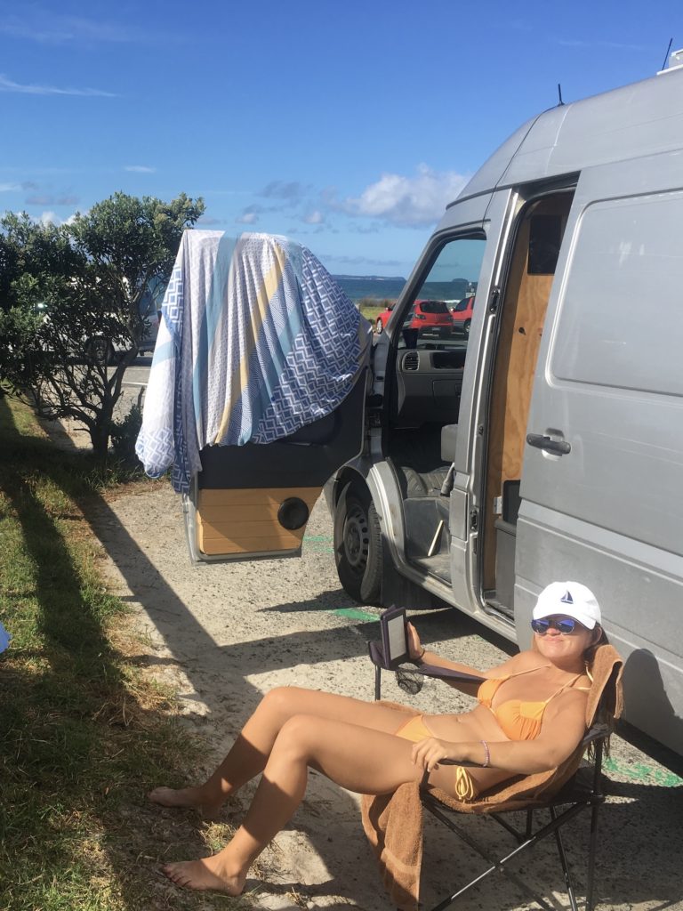 Travel New Zealand on a budget: Niki sits in front of the van at the beach