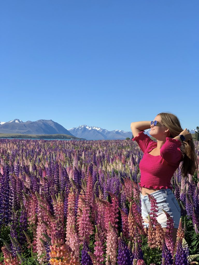 Niki stands in a field of pink and purple lupins, Lake Tekapo, New Zealand