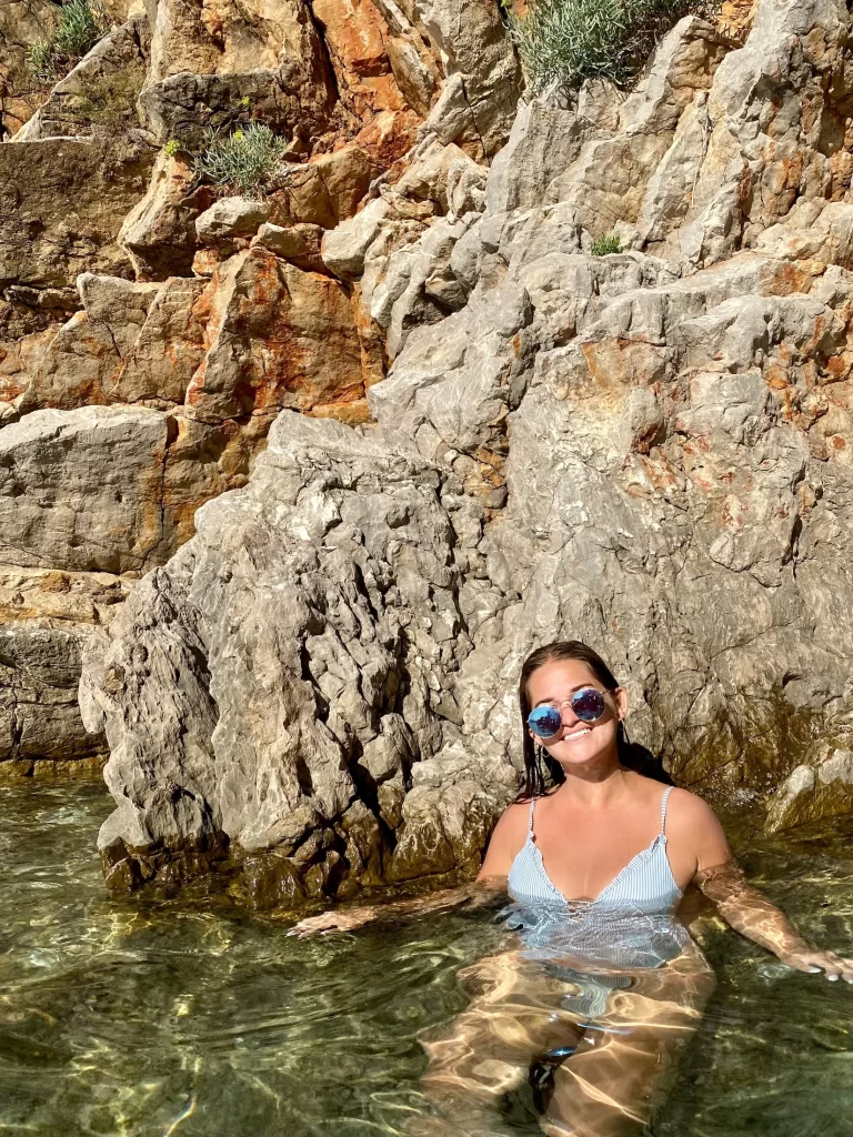 Niki floats in the water in front of a large rocky cliff in Budva, Montenegro