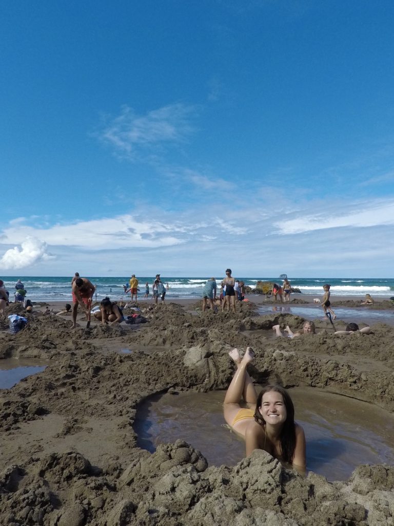 Travel New Zealand on a budget: Niki lies in a hole on Hot Water Beach, Coromandel Peninsula, North Island, New Zealand