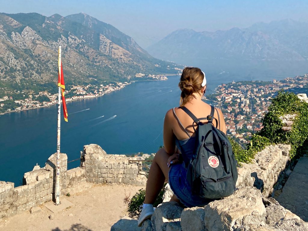 Niki sits in front of view of Kotor, Montenegro from Old Town city walls