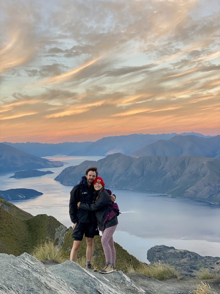 Niki and Ben stand on Roys Peak viewpoint at sunset