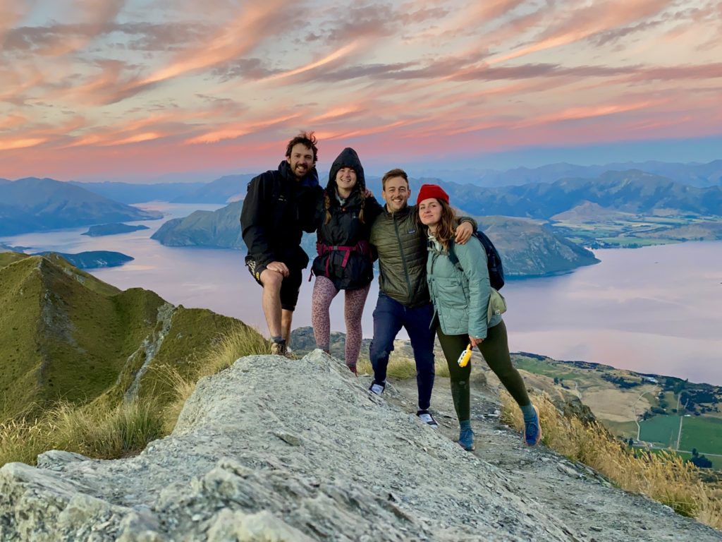 Four friends stand on Roys Peak viewpoint at sunset, Wanaka, New Zealand