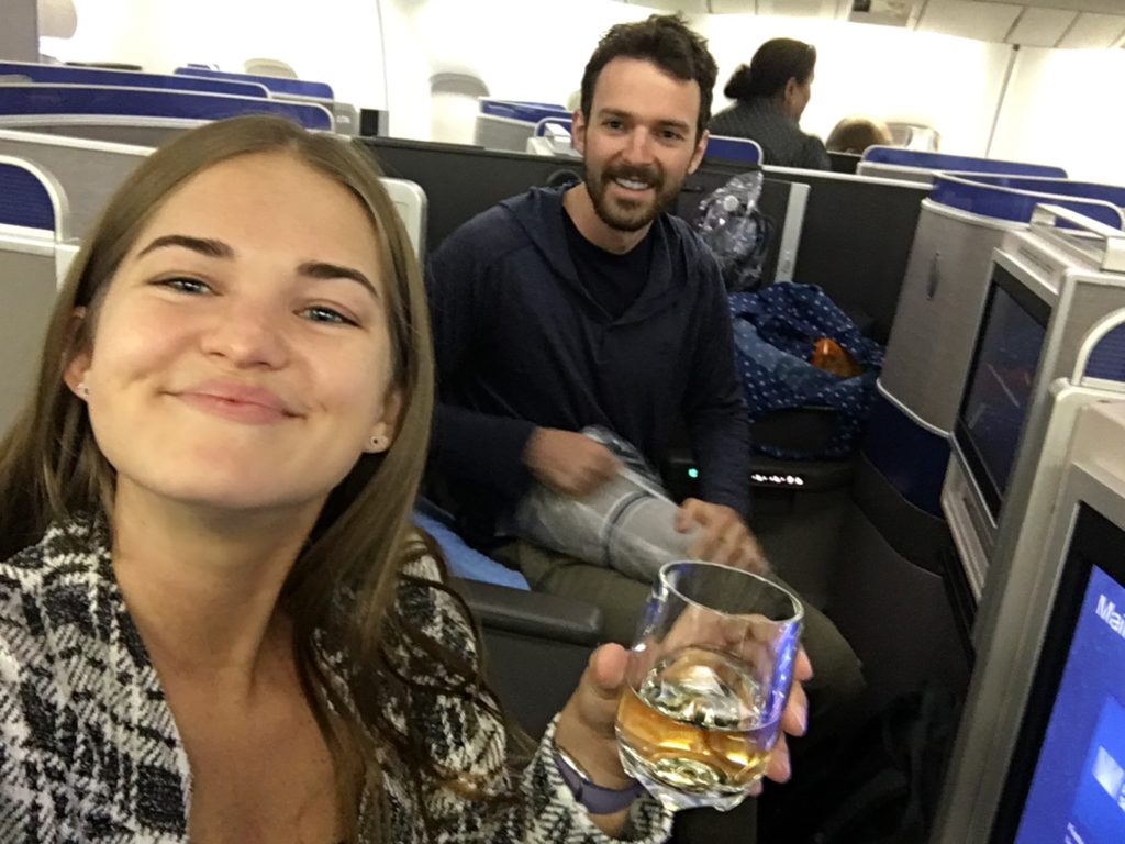 Is business class worth it? Niki and Ben pose in business class with a glass of champagne.