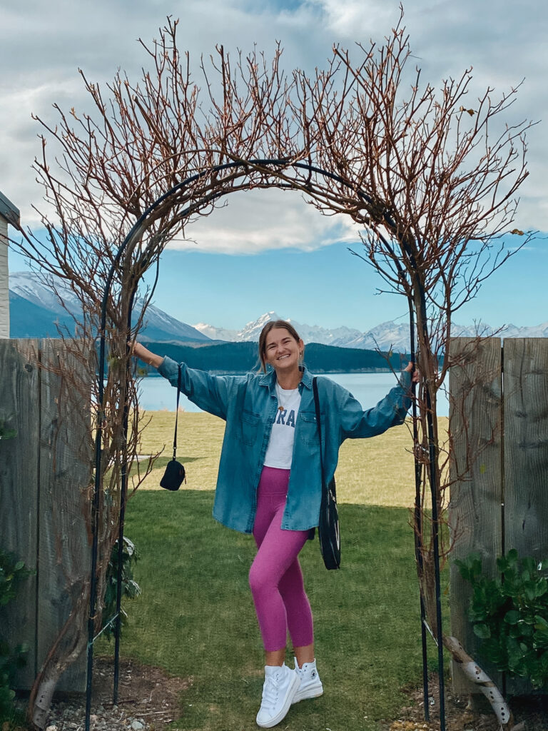 Niki stands in an archway with Lake Pukaki and Aoraki/Mt Cook in the background, Ashley Mackenzie Villa, Mt Cook Lakeside Retreat, South Island New Zealand