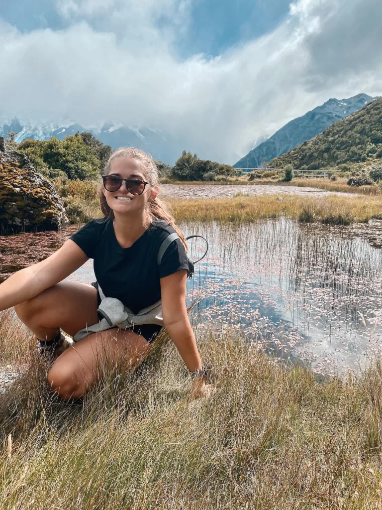 Niki sits near a red lake, Red Tarns Track, Aoraki Mount Cook National Park, New Zealand
