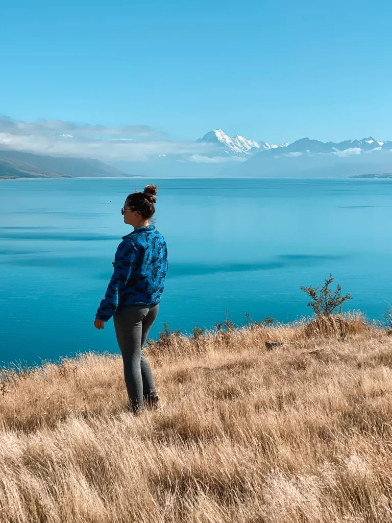 Best day hikes South Island New Zealand: Niki poses on the Pukaki Kettle Hole Track, overlooking Lake Pukaki and Aoraki Mount Cook