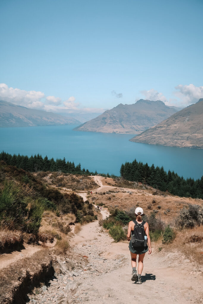 Best day hikes South Island New Zealand: Jamie walks down Queenstown Hill with a view of Queenstown and Lake Wakatipu